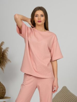 A young woman with blond hair wearing organic cotton pink t-shirt and pink straight leg trousers
