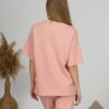 A young woman with blond hair wearing organic cotton pink t-shirt and pink straight leg trousers
