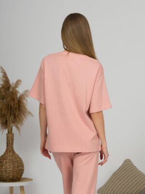 A young woman with blond hair wearing organic cotton pink t-shirt and pink straight leg trousers