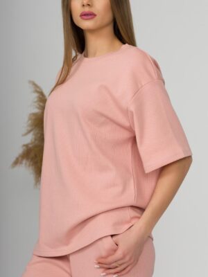 A young woman with blond hair wearing organic cotton pink t-shirt and pink straight leg trousers