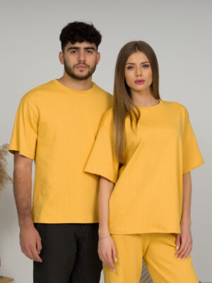 A young woman with blond hair wearing organic cotton yellow t-shirt and yellow straight leg trousers and a young man with black hair wearing organic cotton yellow t-shirt and black trousers