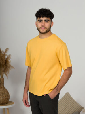 a young man with black hair wearing organic cotton yellow t-shirt and black trousers