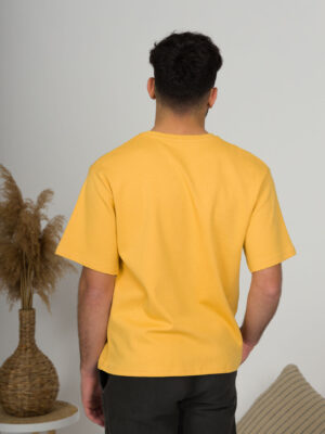 a young man with black hair wearing organic cotton yellow t-shirt and black trousers