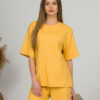 A young woman with blond hair wearing organic cotton yellow t-shirt and yellow straight leg trousers
