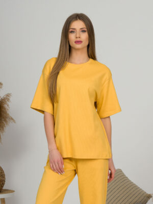 A young woman with blond hair wearing organic cotton yellow t-shirt and yellow straight leg trousers