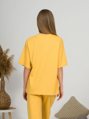 A young woman with blond hair wearing organic cotton yellow t-shirt and yellow straight leg trousers