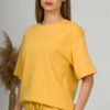 A young woman with blond hair wearing organic cotton yellow t-shirt and yellow straight leg trousers