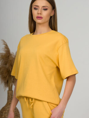 A young woman with blond hair wearing organic cotton yellow t-shirt and yellow straight leg trousers