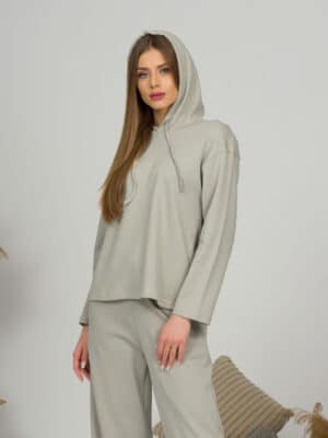A young woman with blond hair wearing organic cotton hooded blouse and straight leg trousers in gray color