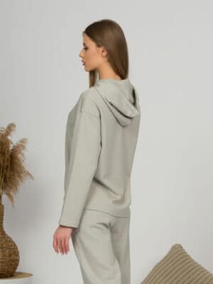 A young woman with blond hair wearing organic cotton hooded blouse and straight leg trousers in gray color