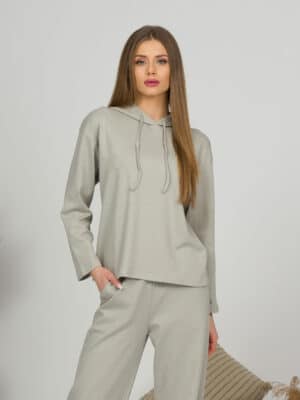 A young woman with blond hair wearing organic cotton hooded blouse and straight leg trousers in gray color
