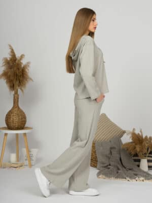 A young woman with blond hair wearing organic cotton hooded blouse and straight leg trousers in gray color