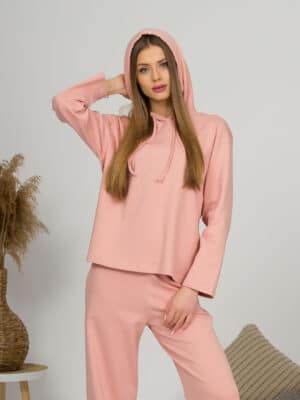 A young woman with blond hair wearing organic cotton hooded blouse and long pants in pink color