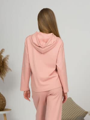 A young woman with blond hair wearing organic cotton hooded blouse and long pants in pink color