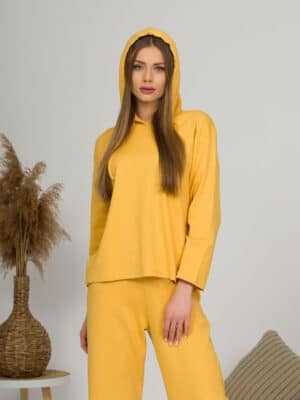 A young woman with blond hair wearing organic cotton hooded blouse and straight leg trousers in yellow color