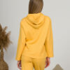 A young woman with blond hair wearing organic cotton hooded blouse and straight leg trousers in yellow color