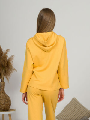 A young woman with blond hair wearing organic cotton hooded blouse and straight leg trousers in yellow color