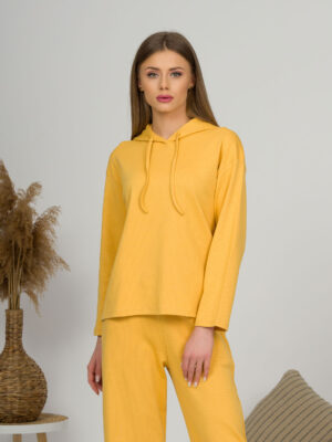 A young woman with blond hair wearing organic cotton hooded blouse and straight leg trousers in yellow color