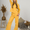A young woman with blond hair wearing organic cotton hooded blouse and straight leg trousers in yellow color