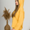 A young woman with blond hair wearing organic cotton hooded blouse and straight leg trousers in yellow color
