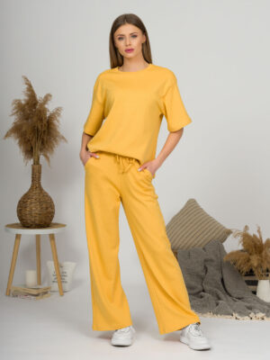 A young woman with blond hair wearing organic cotton yellow t-shirt and yellow straight leg trousers