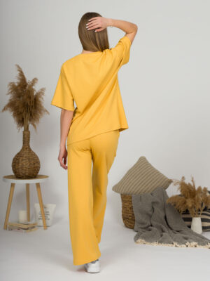 A young woman with blond hair wearing organic cotton yellow t-shirt and yellow straight leg trousers