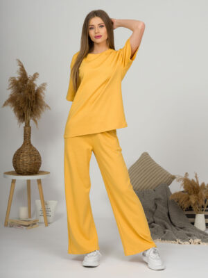 A young woman with blond hair wearing organic cotton yellow t-shirt and yellow straight leg trousers