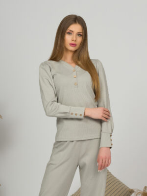 A young woman with blond hair wearing organic cotton blouse with coconut buttons and straight leg trousers in gray color