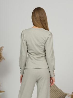A young woman with blond hair wearing organic cotton blouse with coconut buttons and straight leg trousers in gray color