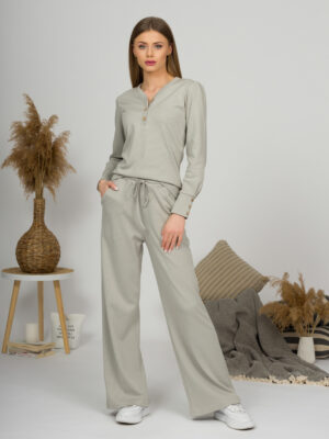 A young woman with blond hair wearing organic cotton blouse with coconut buttons and straight leg trousers in gray color
