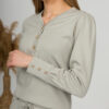 A young woman with blond hair wearing organic cotton blouse with coconut buttons and straight leg trousers in gray color
