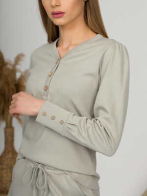 A young woman with blond hair wearing organic cotton blouse with coconut buttons and straight leg trousers in gray color