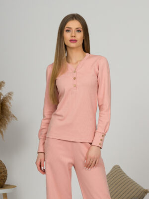 A young woman with blond hair wearing organic cotton blouse with coconut buttons and straight leg trousers in pink color