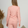 A young woman with blond hair wearing organic cotton blouse with coconut buttons and straight leg trousers in pink color