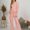 A young woman with blond hair wearing organic cotton blouse with coconut buttons and straight leg trousers in pink color