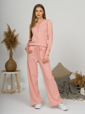A young woman with blond hair wearing organic cotton blouse with coconut buttons and straight leg trousers in pink color