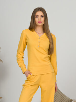 A young woman with blond hair wearing organic cotton blouse with coconut buttons and straight leg trousers in yellow color