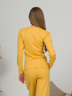 A young woman with blond hair wearing organic cotton blouse with coconut buttons and straight leg trousers in yellow color