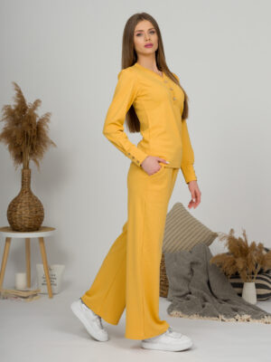A young woman with blond hair wearing organic cotton blouse with coconut buttons and straight leg trousers in yellow color