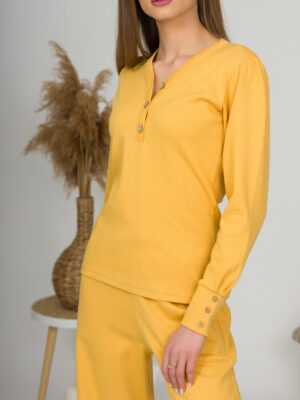 A young woman with blond hair wearing organic cotton blouse with coconut buttons and straight leg trousers in yellow color