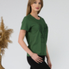 A young woman with blond hair wearing organic cotton green color t-shirt with colored print and black trousers