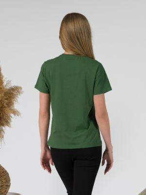 A young woman with blond hair wearing organic cotton green color t-shirt with colored print and black trousers
