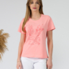 A young woman with blond hair wearing organic cotton peach color t-shirt with print and white trousers