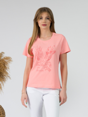 A young woman with blond hair wearing organic cotton peach color t-shirt with print and white trousers