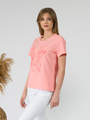 A young woman with blond hair wearing organic cotton peach color t-shirt with print and white trousers