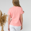 A young woman with blond hair wearing organic cotton peach color t-shirt with print and white trousers