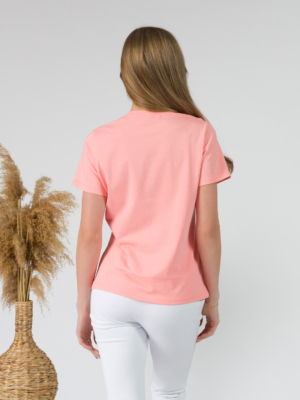 A young woman with blond hair wearing organic cotton peach color t-shirt with print and white trousers
