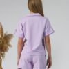 Young woman with blond hair wearing organic cotton violet blouse t-shirt and organic cotton violet shorts