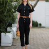 Young woman with blond hair wearing black organic cotton 7/8 length short sleeve jumpsuit with side pockets and coconut buttons