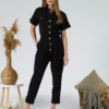 Young woman with blond hair wearing black organic cotton 7/8 length short sleeve jumpsuit with side pockets and coconut buttons